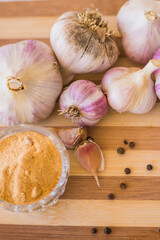 A beautiful and large garlic lies with peppercorns and garlic seasoning on a brown wooden board.
