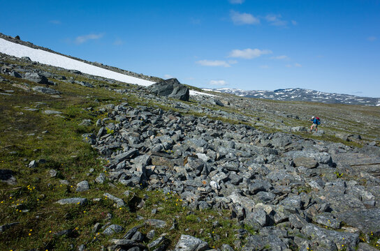 Hiking in Swedish Lapland. Man traveler trekking alone Nordkalottruta or Arctic Trail in northern Sweden. Arctic nature of Scandinavia in warm summer sunny day with blue sky, rocks and snow