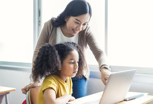 Happy Asian Female Teacher Helping School Kids Using Laptop Computers In IT Class. Education, Elementary School, Learning And Technology Concept.