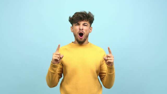 Young arab man pointing up, looking surprised and amazed, is presenting a product