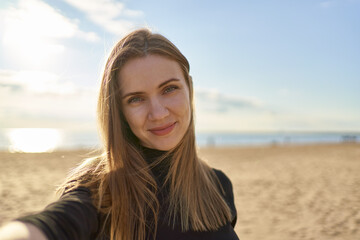 Pretty female with long hair looking at camera and smiling in sunny evening in ocean or sea...
