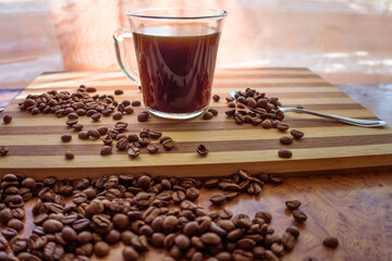 On a wooden plank there is a cup of custard coffee and fried arabica beans from which coffee was brewed.