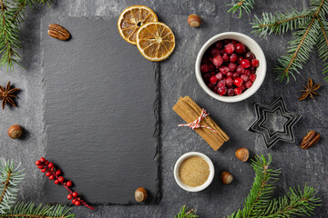 Obraz na płótnie Canvas Culinary background with christmas winter spices and ingredients for baking on dark stone table with a black slate with chalkboard for your text. Top view. Copy space.