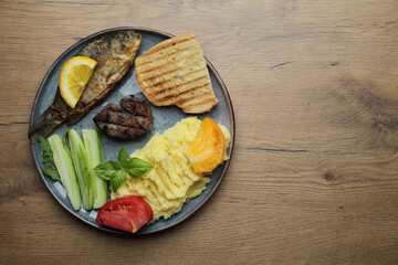 Fried fish, meat steak and vegetables on a plate. On a wooden table