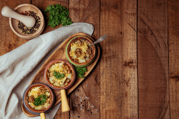  Baked potatoes with mushrooms under cheese crust in portioned pots on wooden textured background
