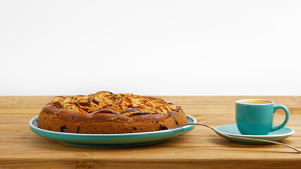 Homemade pie with apples and plums with almond petals and cup of coffee espresso on wooden table.
