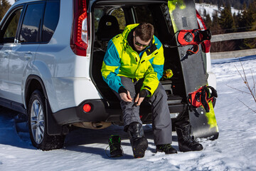 man sitting in car trunk changing for snowboard