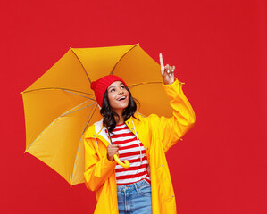 Happy ethnic female with umbrella pointing up.