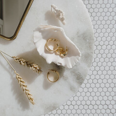 Minimal fashion composition with golden earrings in seashell on marble table with mirror and wheat stalks. Flat lay, top view bijouterie / jewelry concept on mosaic tile background. - obrazy, fototapety, plakaty