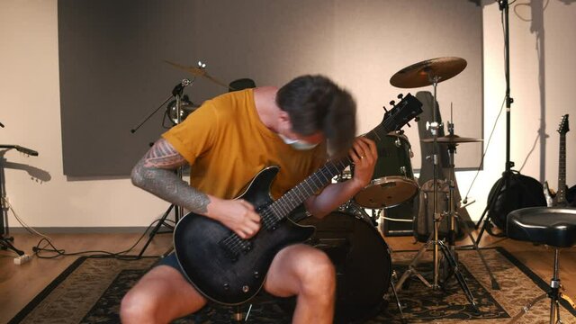 Professional music studio. Man playing guitar. Life of musicians throughout the coronavirus. The caucasian male person wearing the health mask throughout the COVID-19 times. 