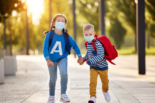 Cheerful siblings in protective masks with school backpacks.