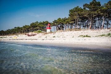 white sand beach with blue water an red white lighthouse