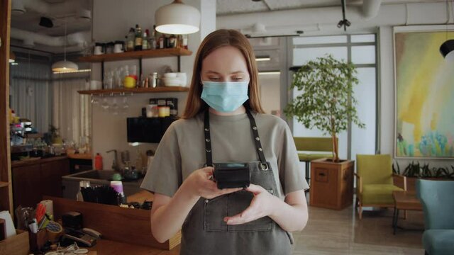 Barista medical face mask in coffee shop, lockdown, quarantine, coronavirus is over, back to normal concept. Woman girl buy or purchase coffee contactless, banking terminal nfc payment by phone