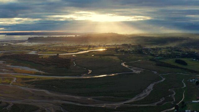 aerial view of wetlands and delta of the Chamiza river at its mouth to the bosom of Reloncavi, in a cloudy sunset with sun rays crossing the clouds