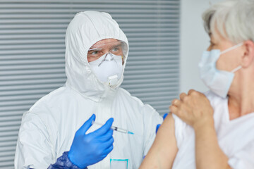 Professional doctor wearing gloves giving antiviral injection to aged woman sitting in front of him in hospital ward