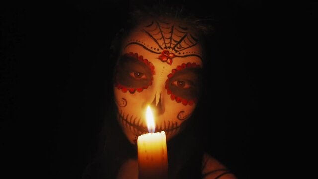 Halloween portrait of a girl with skeleton makeup. The girl looks at a burning candle