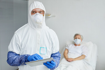 Horizontal medium portrait of modern doctor wearing protective uniform with mask, gloves and eyewear holding digital tablet