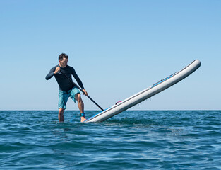 Young active man making pivot or step back turn trick on stand-up paddle board on sea water
