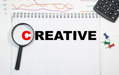 CREATIVE in a magnifying glass on a notepad against the background of graphs, calculator and paper...