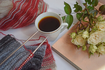 A Cup of fragrant coffee and a knitted scarf with knitting needles on a white background.