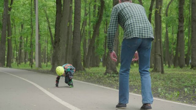 Father and son are preparing for roller skating in the fresh air. father's day. The son learns to roller skating, falls and gets up.