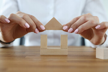 Female hands build house from wooden cubes. The influence of a woman on the atmosphere in the house...