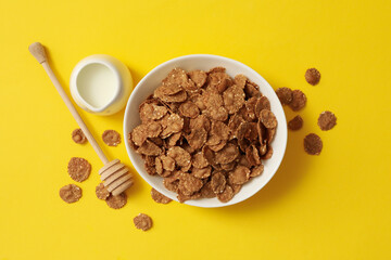 Milk and bowl of muesli on yellow background, top view