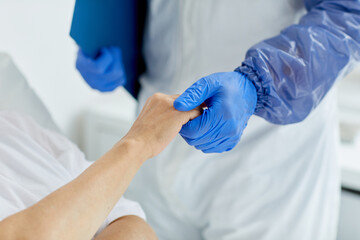 Unrecognizable doctor wearing protective gloves holding hand of senior woman in hospital ward