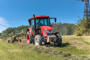 Modern red tractor in the agricultural field. Work on an organic farm. Haymaking. Tractor on a green field.