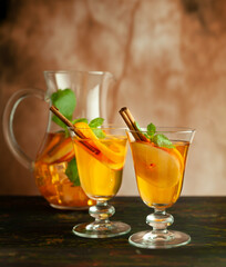 Apple cider cocktail with red oranges and spices in glasses and jug on table. Concept of autumn and winter drinks.