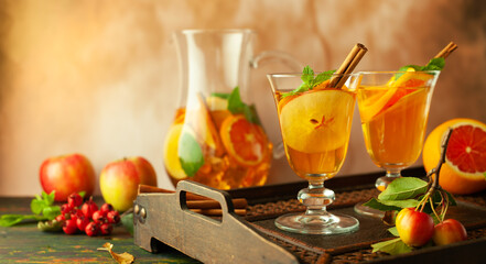 Apple cider cocktail with red oranges and spices in glasses and jug on table. Concept of autumn and winter drinks.