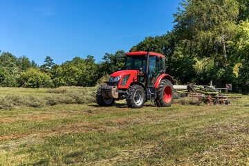 Modern red tractor in the agricultural field. Work on an organic farm. Haymaking. Tractor on a green field.
