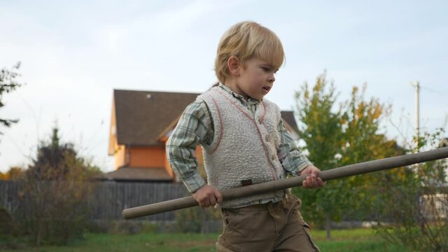 Little Child Rakes Leaves. Boy Helps Cleaning in House Backyard. Autumn Evening Rural Scene. Slow motion