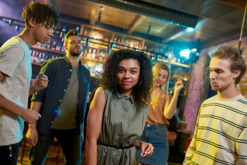 Feel the song. Attractive mixed race young woman smiling at camera while having fun, dancing in the night club surrounded by friends