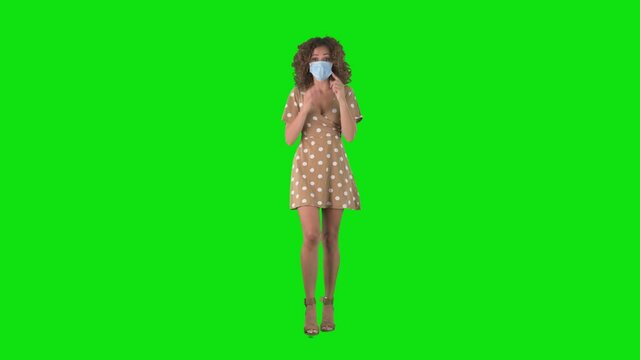 Young happy woman with face mask walks meet and greet friend on chroma key green screen. 