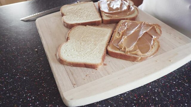 Preparing peanut butter and jelly sandwich on a wood cutting board.