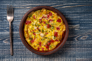 Ceramic bowl with vegetable frittata, simple vegetarian food. Frittata with tomato, pepper, onion and cheese on wooden table, close up