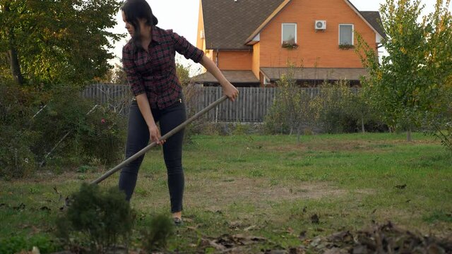 Young Woman Rakes Leaves. Mother with Son and Cat are Cleaning House Backyard. Autumn Evening. Slow motion