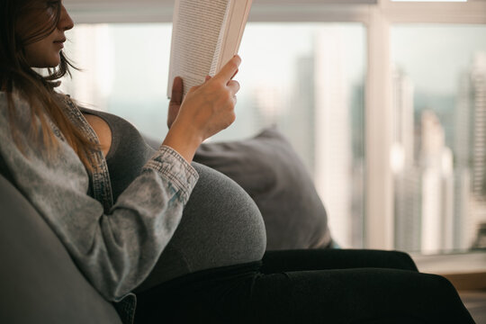 pregnancy concept - pregnant woman on sofa and reading book