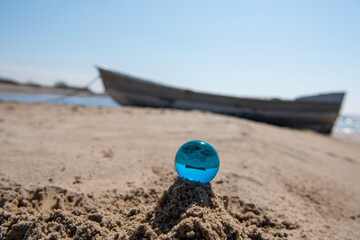Blue glass ball on sand near the sea. Abstract conceptual photo.