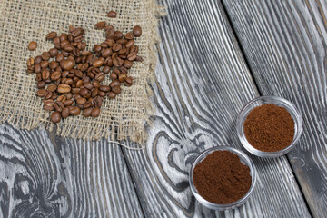 Coffee beans on coarse linen. Ground coffee in containers. On a surface of brushed pine boards painted black and white.