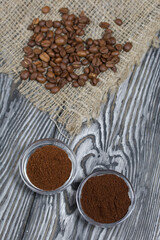 Coffee beans on coarse linen. Ground coffee in containers. On a surface of brushed pine boards painted black and white.