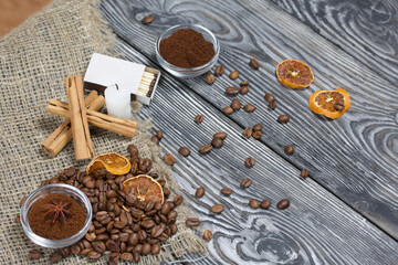 Coffee beans on rough linen and candle stub. Ground coffee in containers and spices. On a surface of brushed pine boards painted black and white.