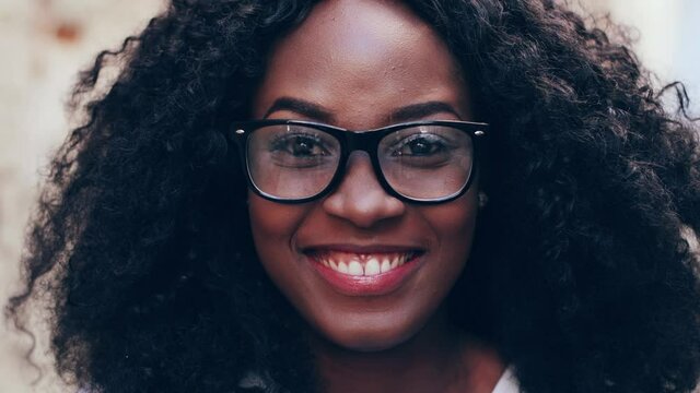 Close up portrait of young african american girl in glasses with curly hair. Beautiful woman with snow-white smile looking at camera.