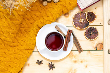 aromatic hot cinnamon tea covered with a warm scarf on a wooden autumn background.