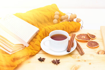 aromatic hot cinnamon tea covered with a warm scarf on a wooden autumn background. comfortable reading a book. sunshine