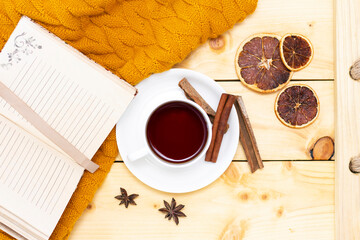 aromatic hot cinnamon tea covered with a warm scarf on a wooden autumn background. comfortable reading a book.