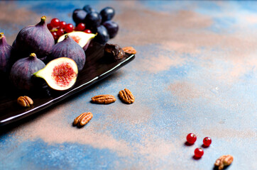 Fresh fig fruits on dark plate with red current, grapes and pecan nuts, copy space