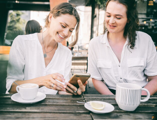 Two young women friends are sitting in a cafe drinking coffee and discussing the news, joyful and happy coffee break