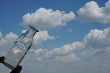 male Hand hold transparent glass bottle. empty bottle fill with blue sky. against blue sky . empty...